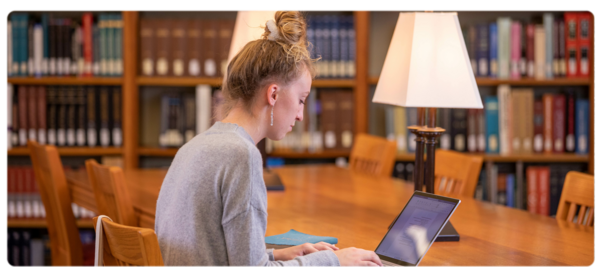 A student works at a laptop at a table in the Peterson Memorial Library.